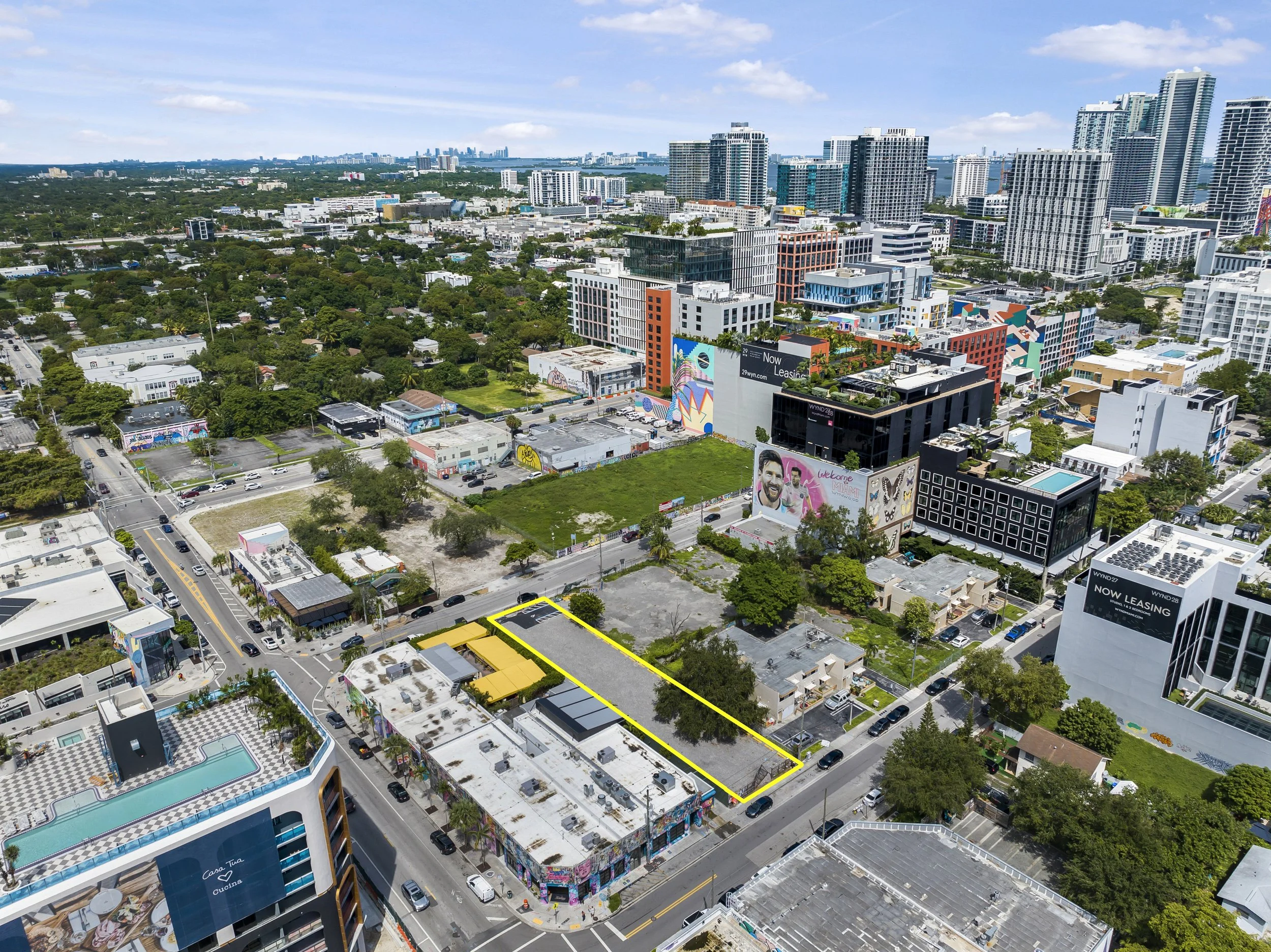 Aerial view of a cityscape showing streets, colorful buildings, green parks, and high-rise office buildings in the background during daytime.