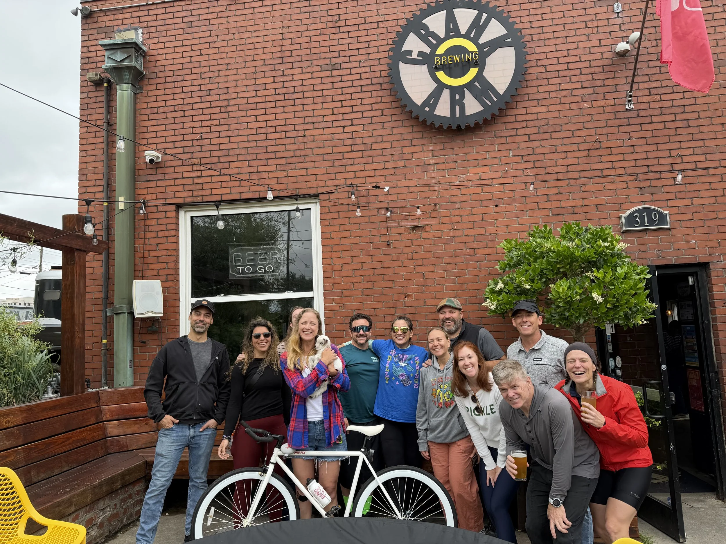 A group of smiling people posing outside a brick building with a round sign that reads 'Cran',
