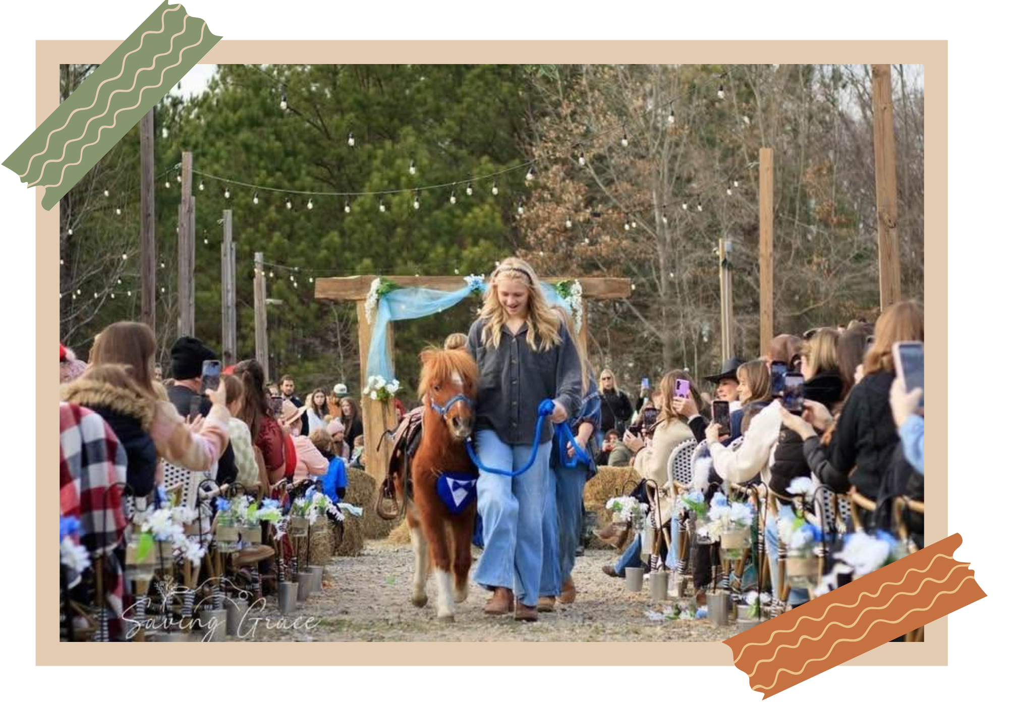 A young woman riding a small pony down the aisle of a wedding ceremony outdoors surrounded by guests. The woman has long blonde hair and is smiling, wearing a dark denim jacket and blue jeans. The aisle is decorated with flower arrangements, and the background features trees with hanging string lights.