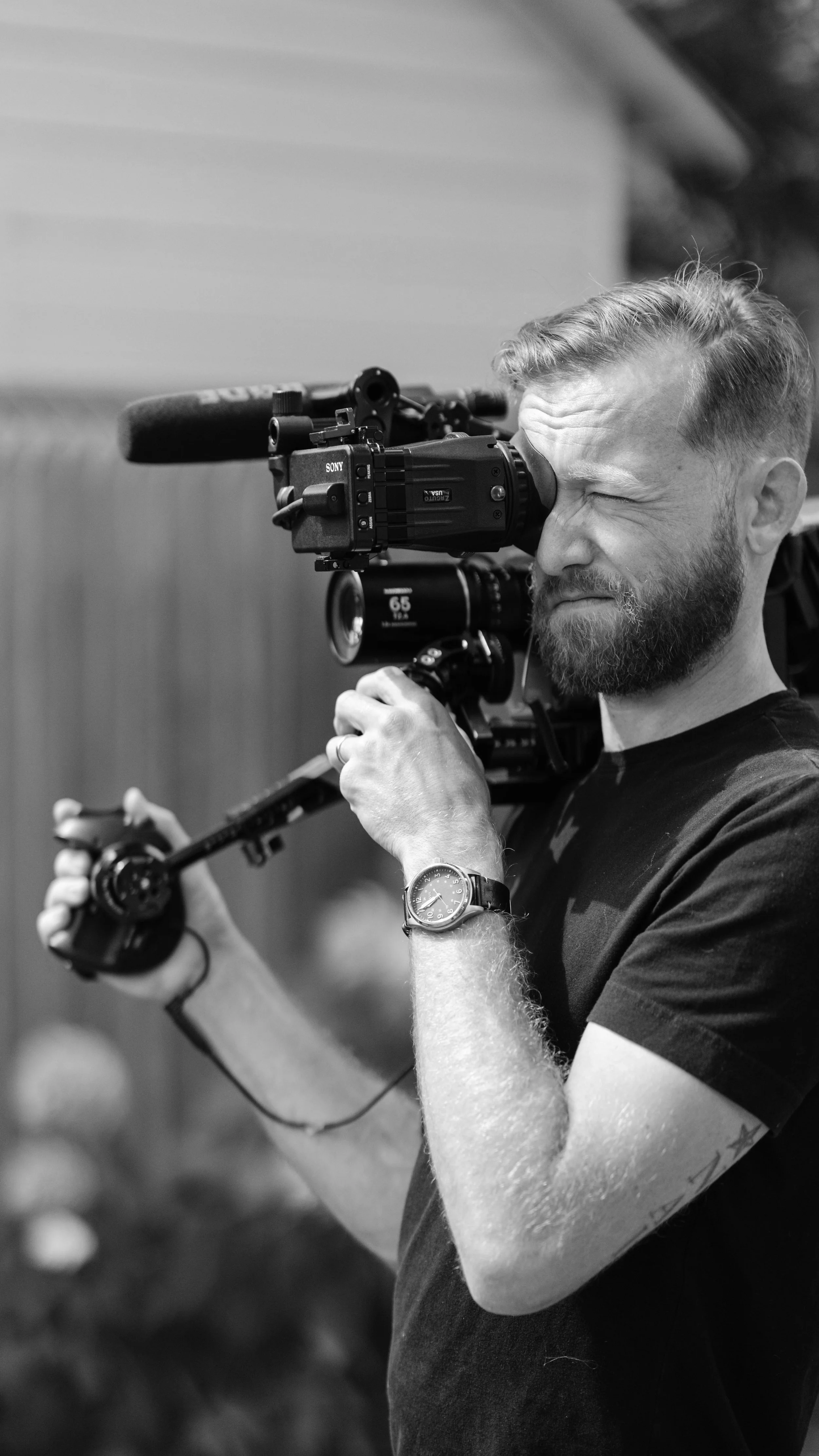 A man holds a camera on his shoulder and looks into viewfinder.