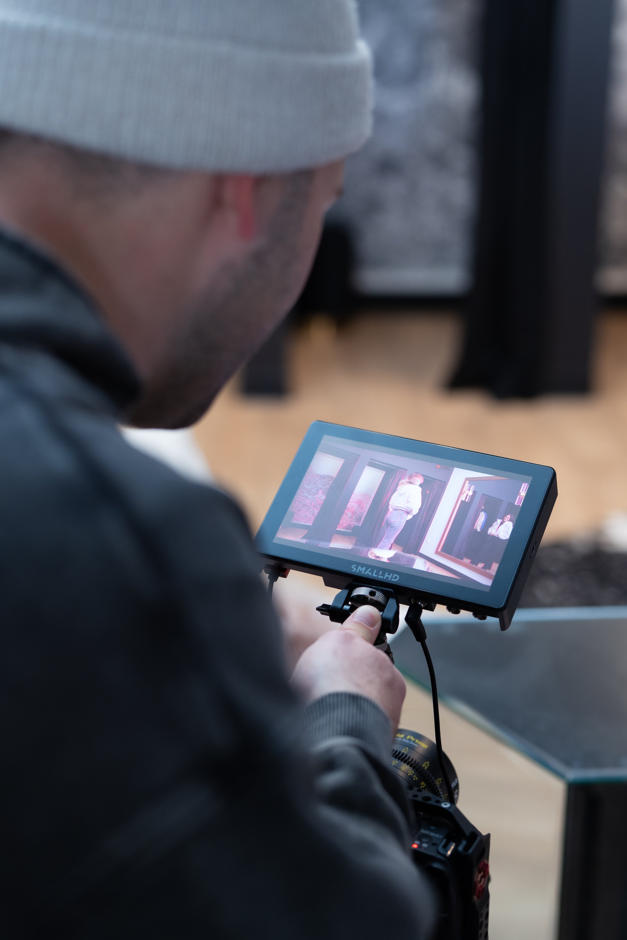 Close-up of a person wearing a gray beanie holding a camera monitor displaying photos of people, with a blurred background.