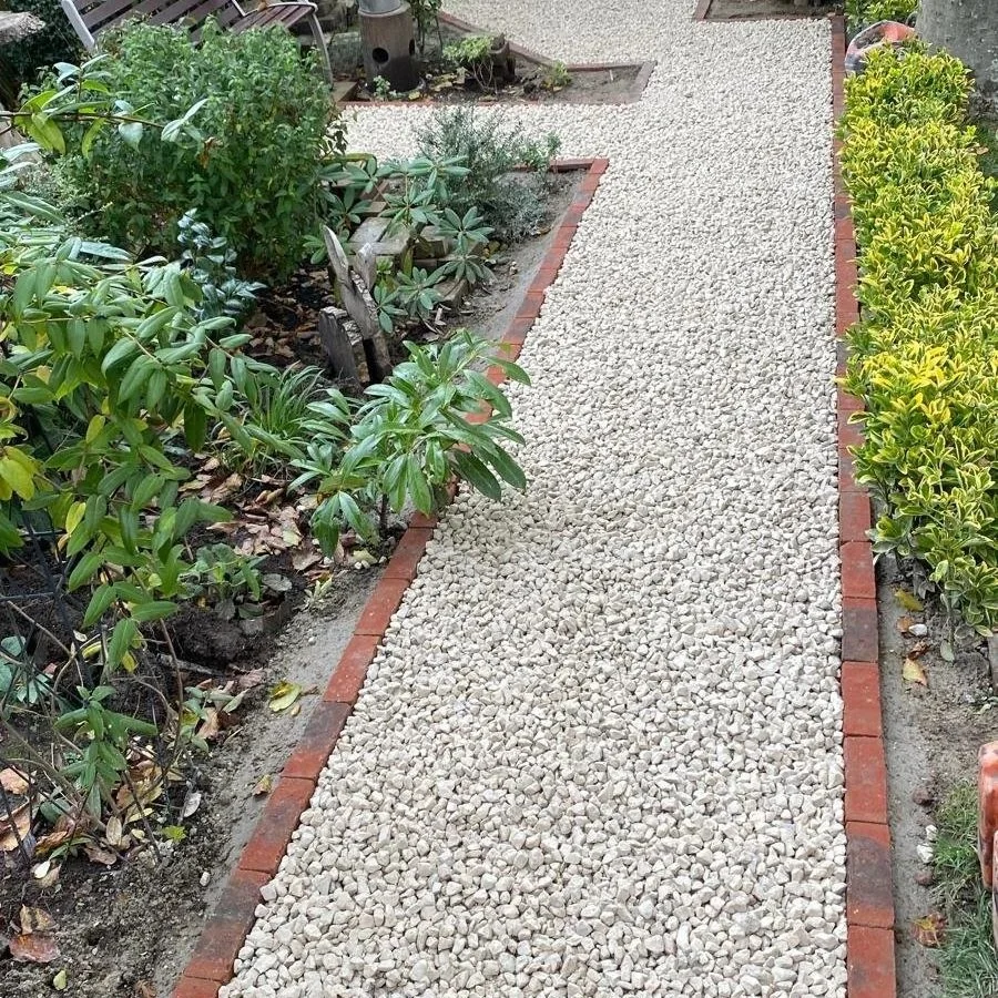 A gravel pathway in a garden with plants and bushes on both sides, edged with red bricks.