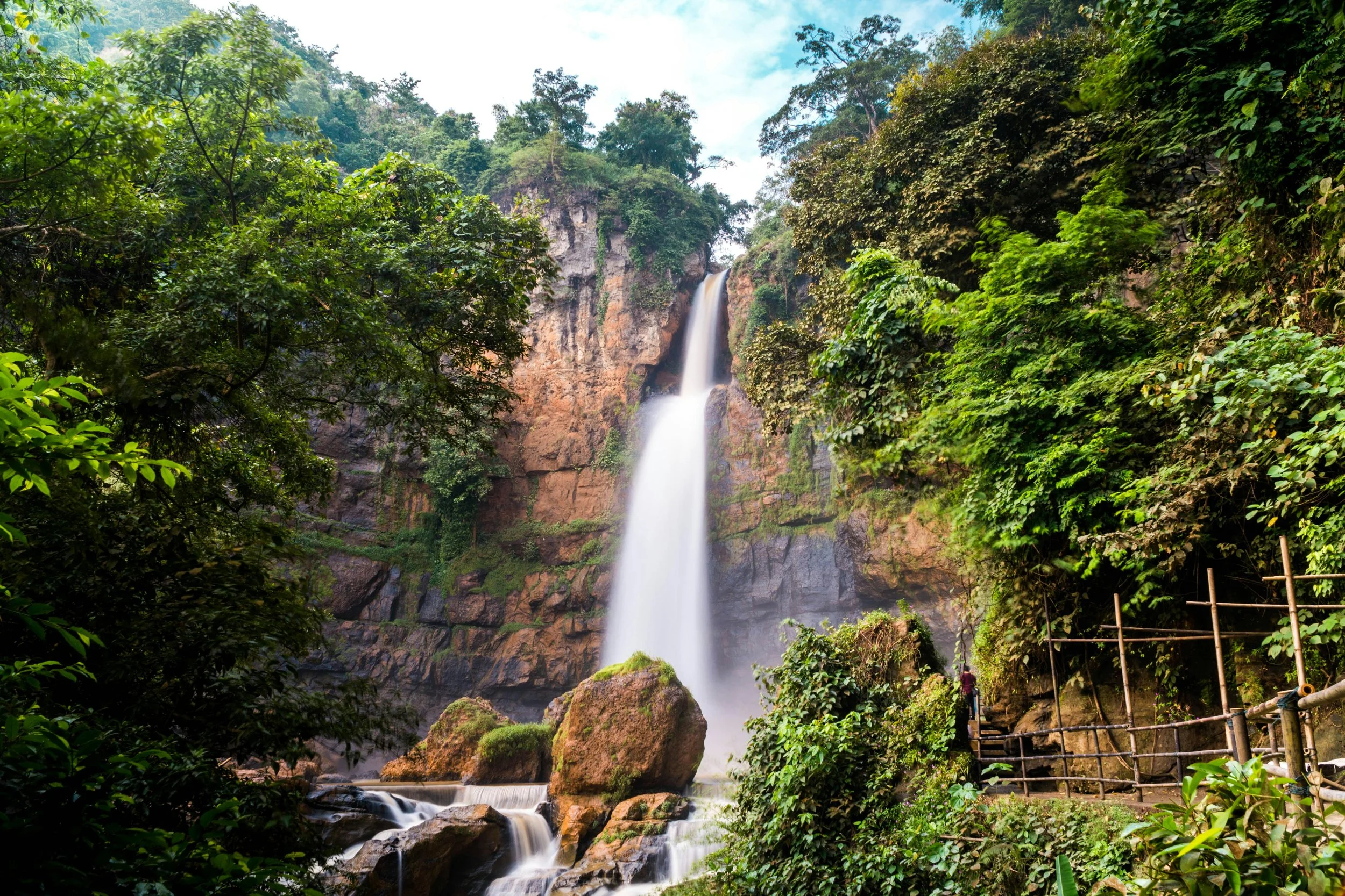 A tall waterfall cascading down a rocky cliff surrounded by lush green trees and foliage.