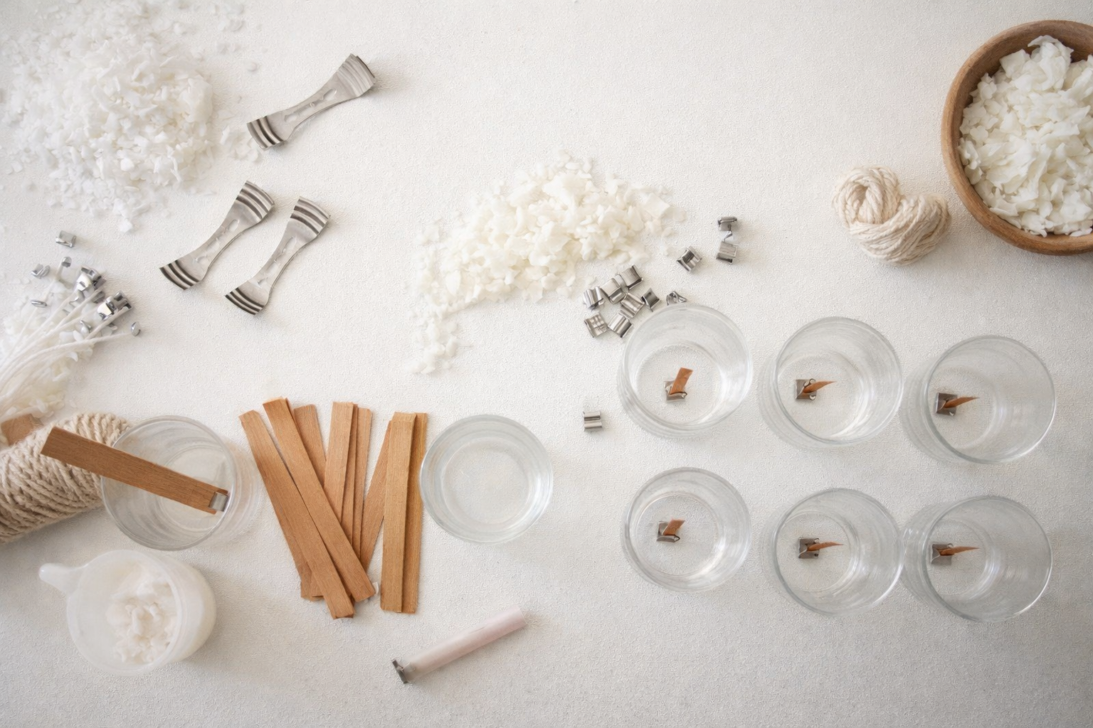 Various candles and candle-making supplies on a white surface, including wax, wicks, a jar of beeswax, and candle containers.