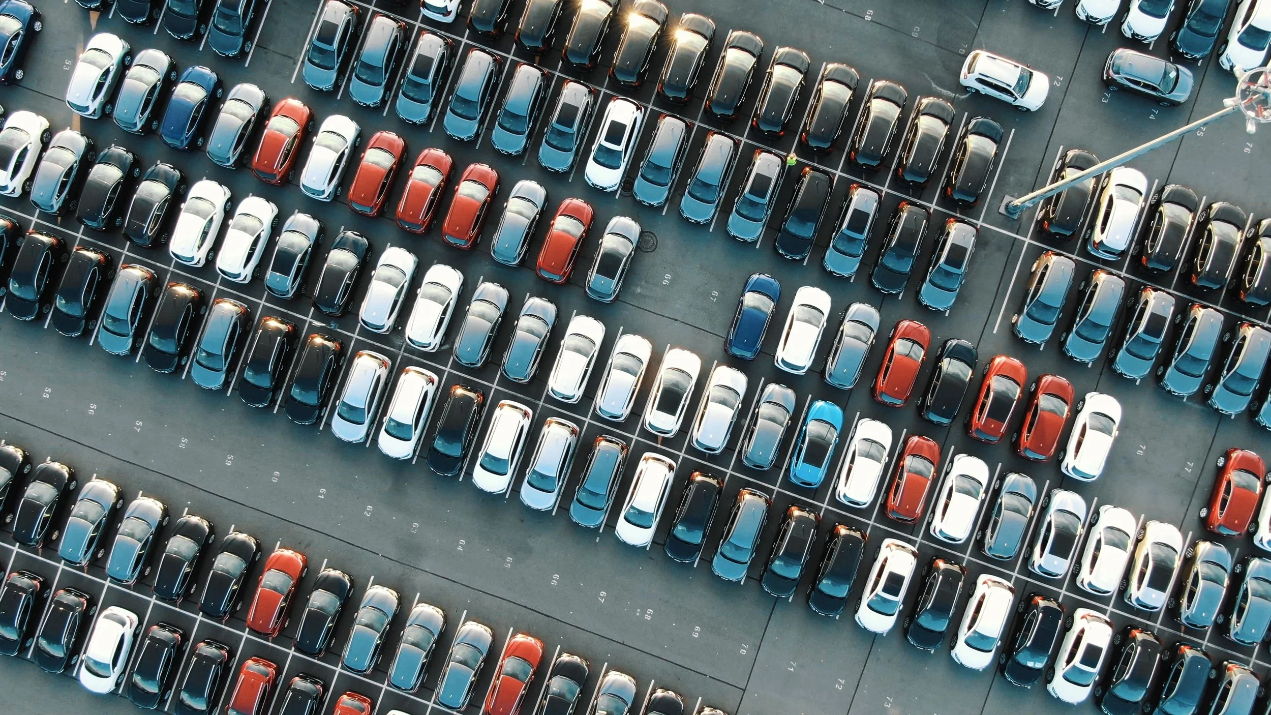 Aerial view of a parking lot filled with various cars, organized in rows with marked parking spaces.
