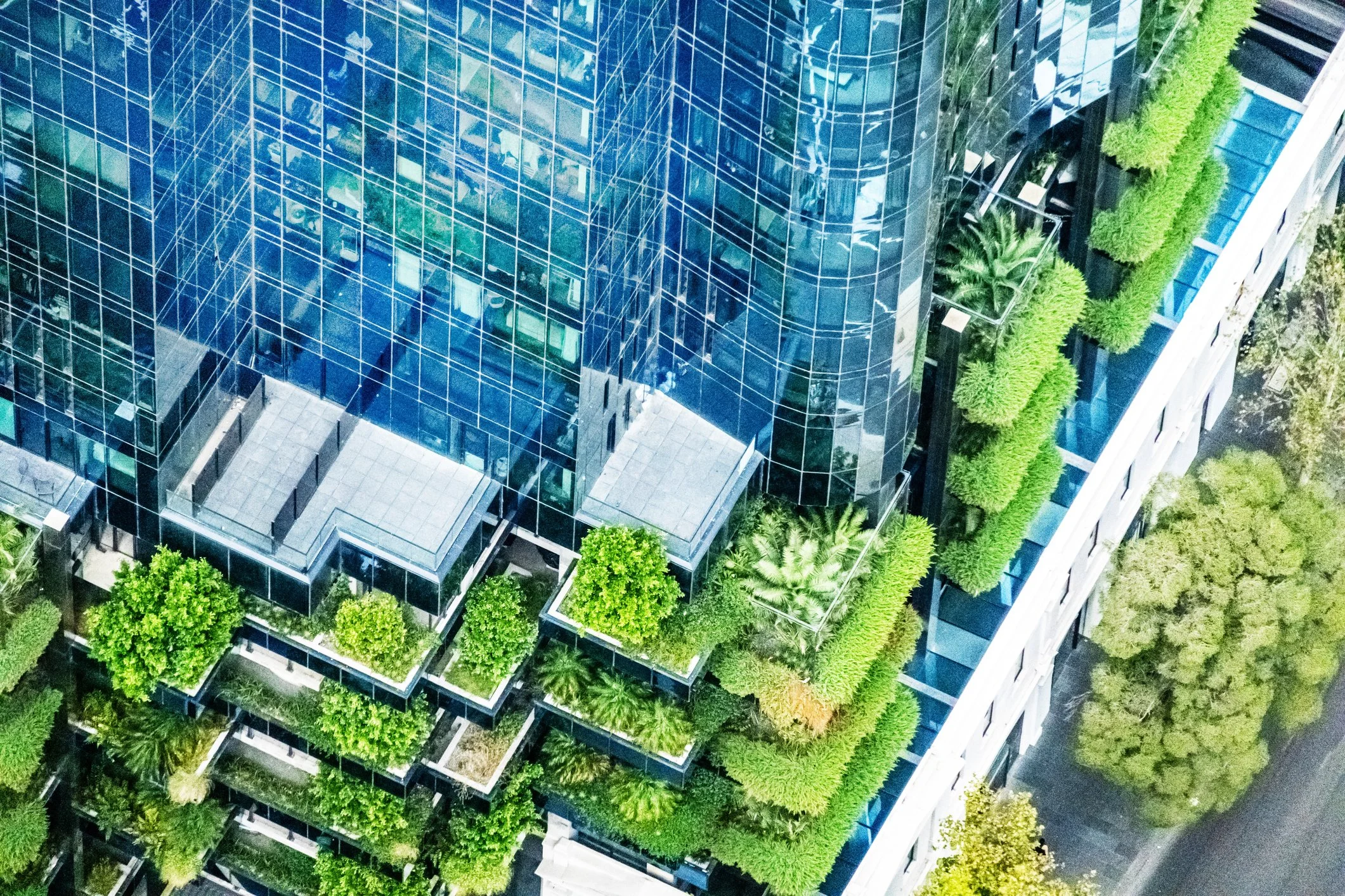 An aerial view of a modern glass office building with green plants and trees on the balconies.