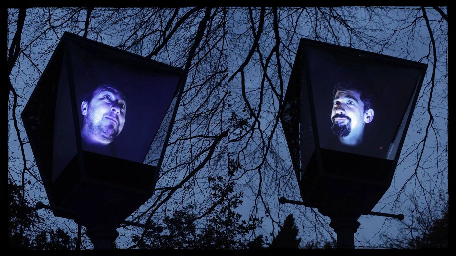 Two streetlamp fixtures with digital screens displaying the faces of two men against a dark, nighttime sky with leafless tree branches.