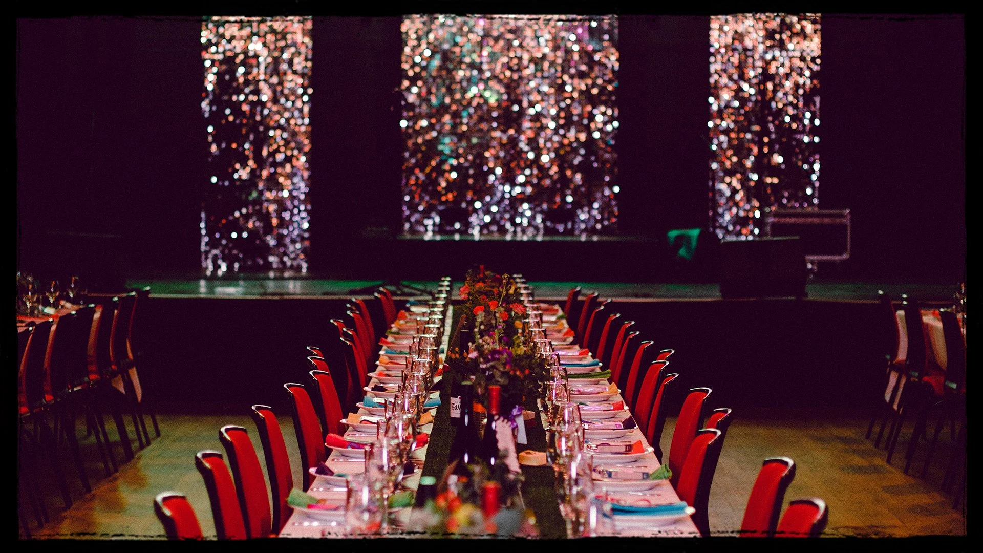 A banquet table set for a formal event with flower arrangements and string lights in the background.