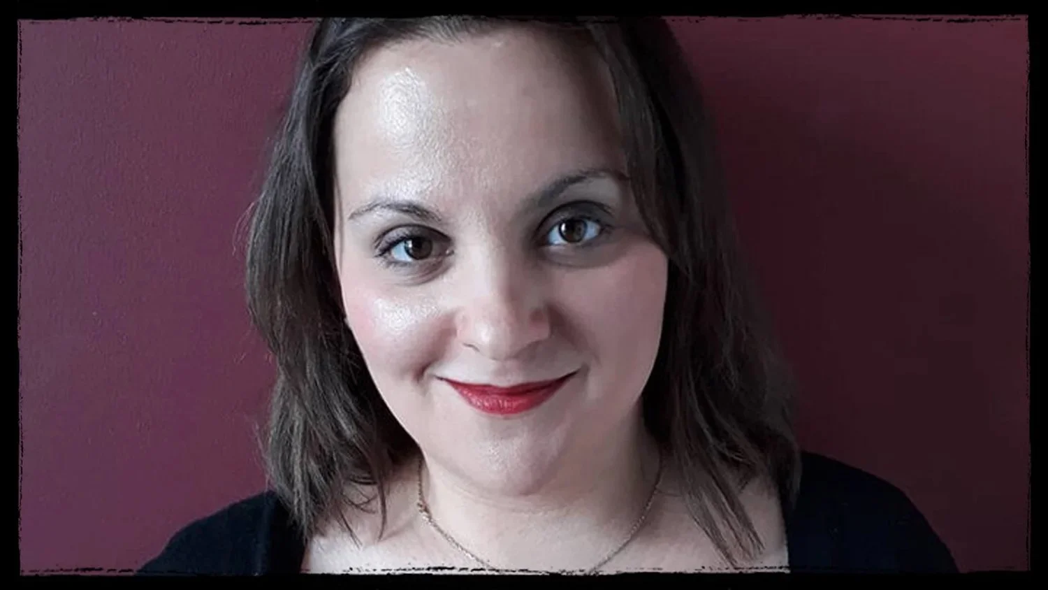 Close-up of a woman with shoulder-length brown hair, wearing makeup including red lipstick, smiling, against a dark red background.