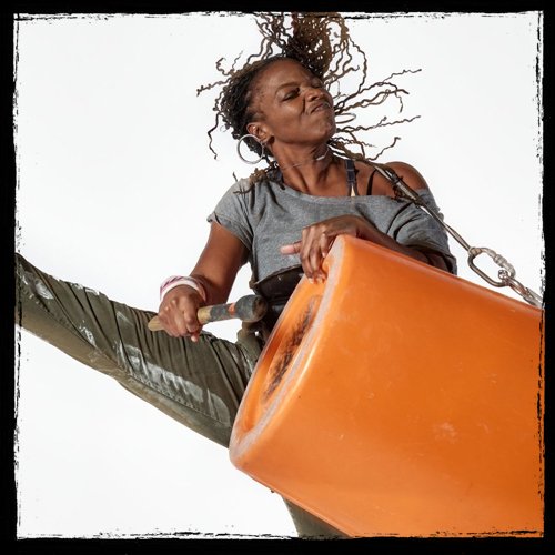 A woman with braided hair and earrings swinging on an orange swing set against a white background.