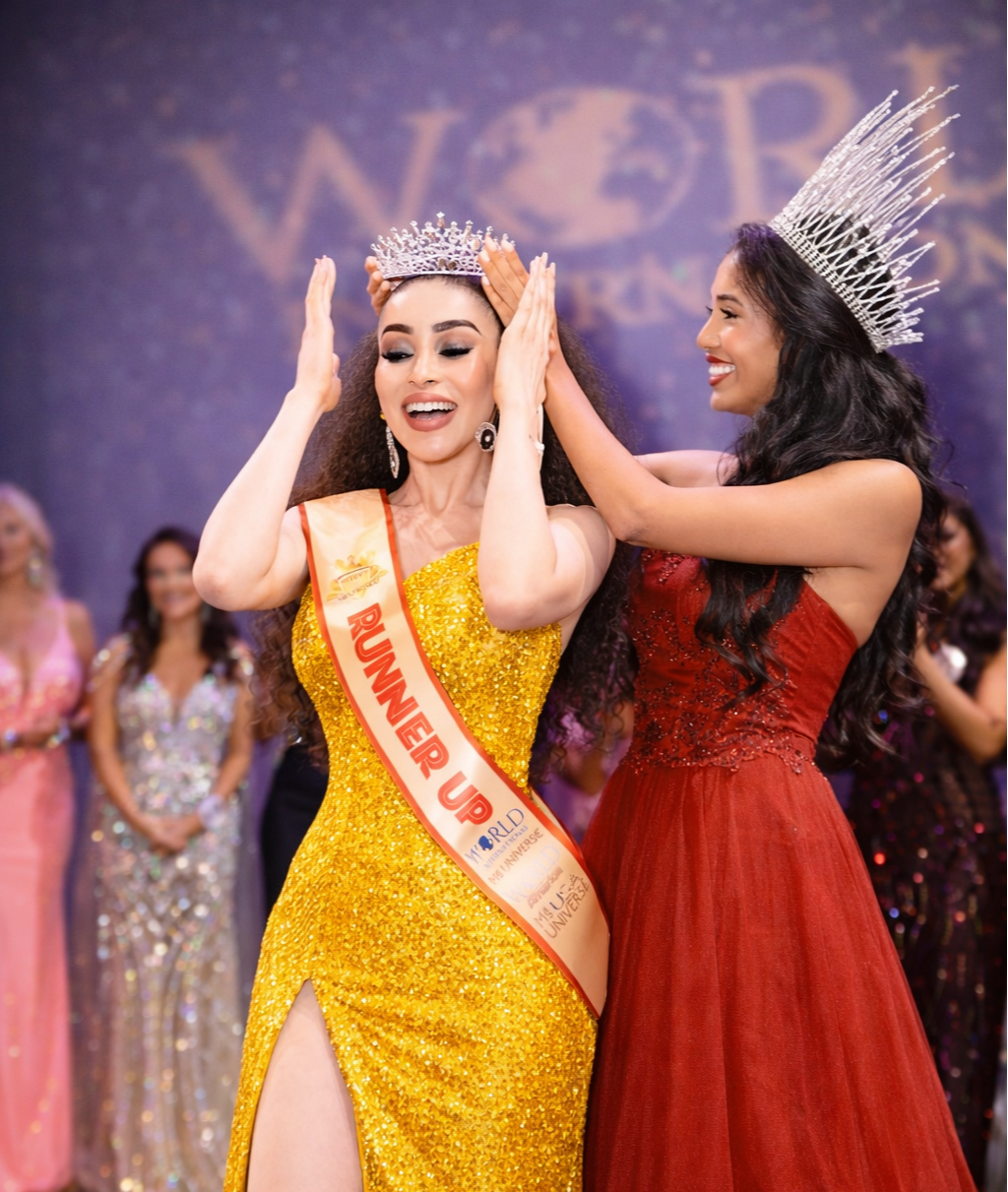 Miss USA winner wearing a crown, yellow gown, and sash saying 'Runner Up' being crowned by another woman in a red gown and silver crown at a beauty pageant.