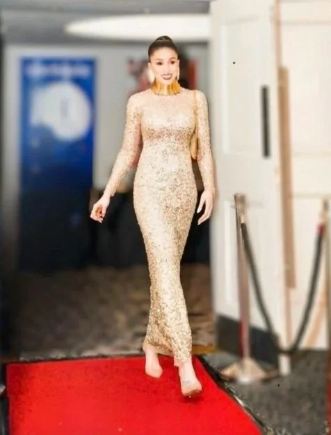 A woman in a long, fitted gold dress walking on a red carpet.