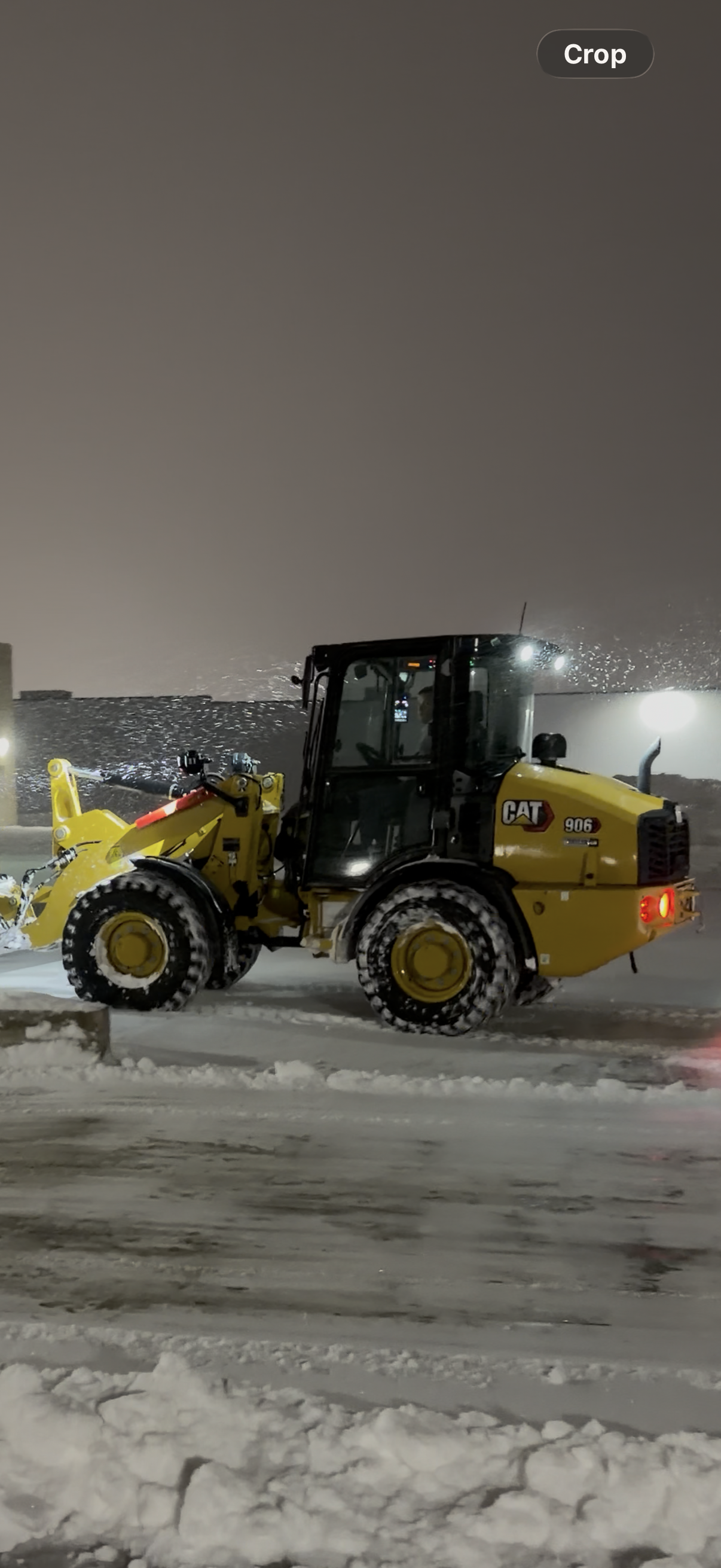 Yellow Caterpillar brand snow plow in operation on a snowy night.