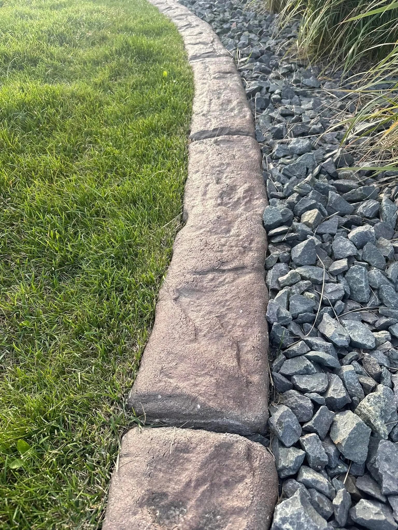 Lawn grass on the left, with a edge of large red brick pavers, and a bed of small gray rocks on the right.