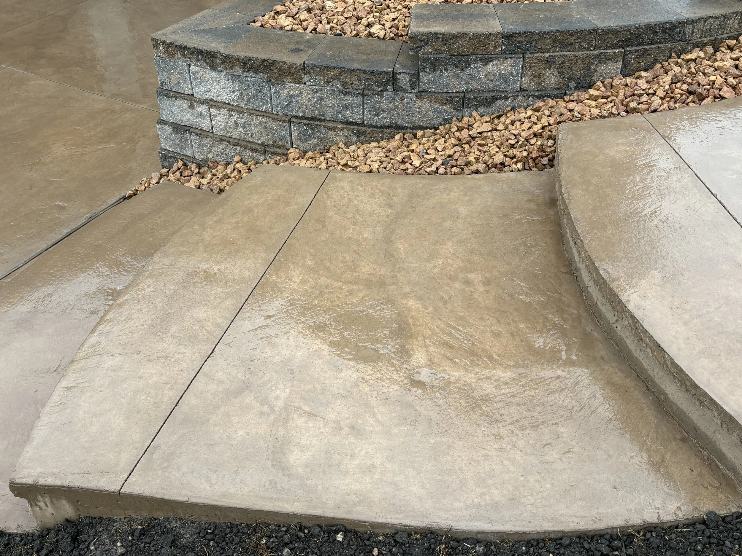 Concrete steps and sidewalk with a stone retaining wall and gravel landscaping in the background.