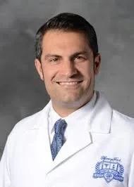 Portrait of a smiling male doctor in white coat against gray background.