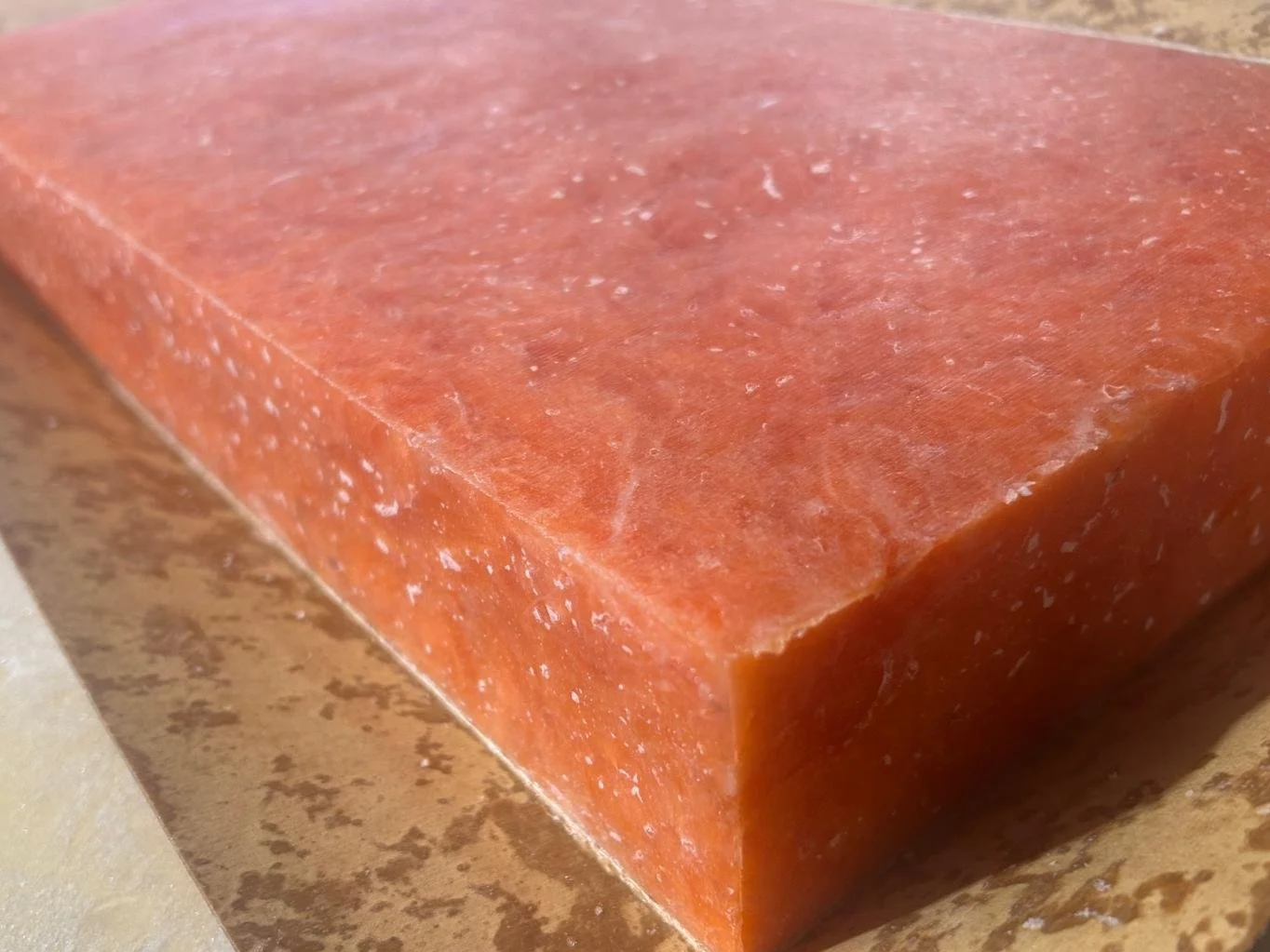 Close-up of a rectangular block of pink Himalayan salt with a coarse texture, resting on a light-colored surface.