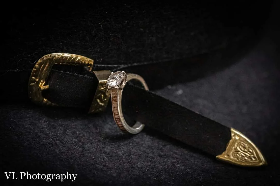 A close-up of a black and gold ring with a clear gemstone and gold decorative tips on a black fabric surface.