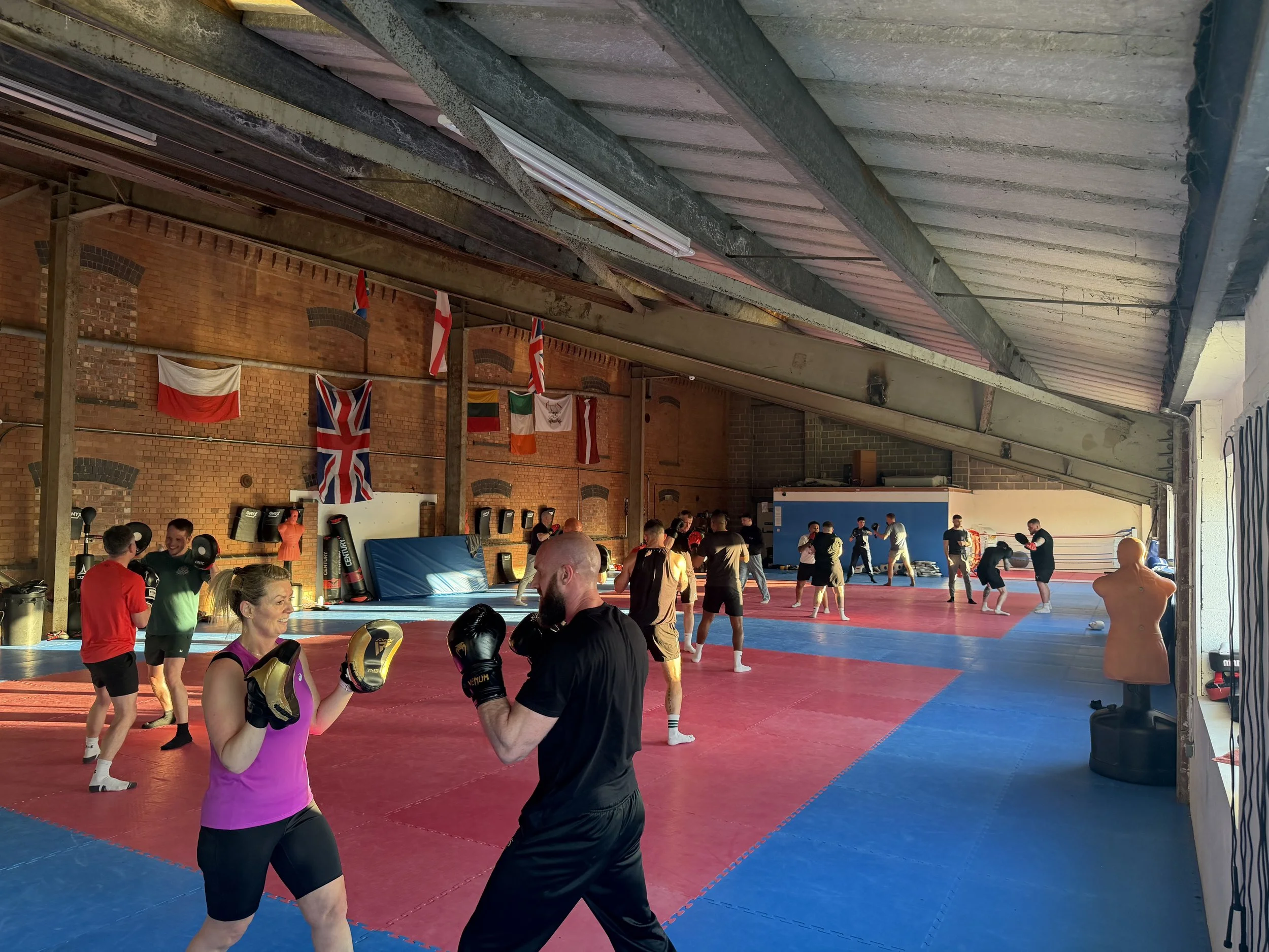 People training and practicing martial arts in a gym with brick walls, flags, and boxing equipment.