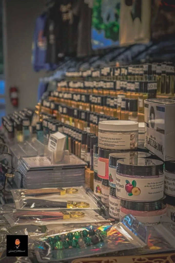 Travel-size beauty and skincare products on display, including jars of moisturizer or body butter among other items. There are also small skincare or cosmetic tools and jewelry, such as earrings, in plastic packaging. The background features shelves 