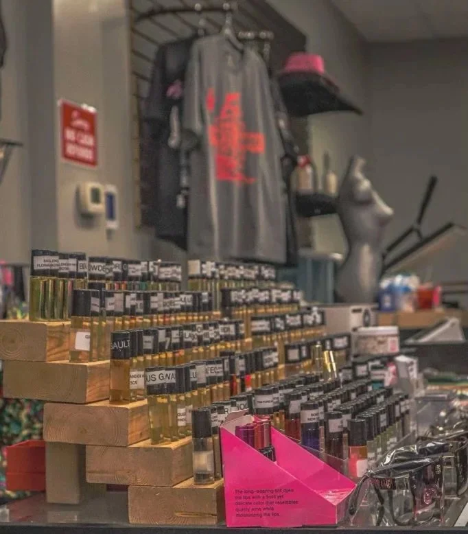 Display of various perfume bottles in a store, with a mannequin torso and clothing in the background.