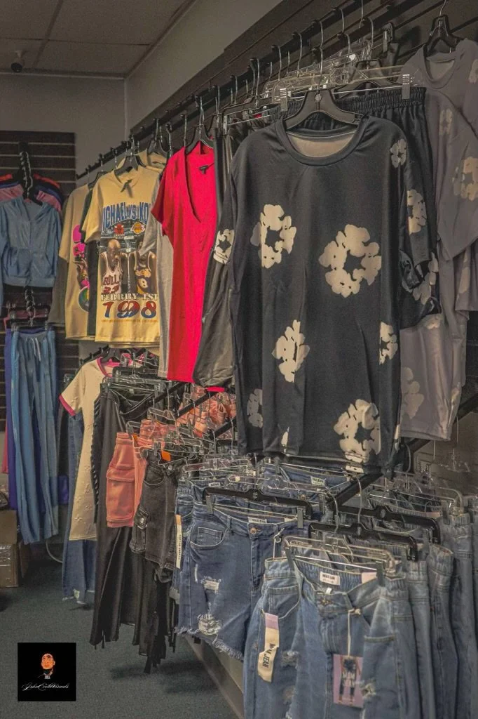 Clothing display featuring various casual wear, including jeans, t-shirts, and tops with floral prints, on hangers in a retail store.