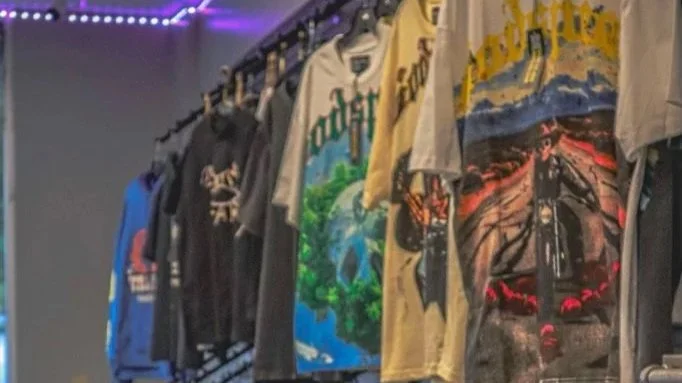 Clothing rack with various t-shirts hanging, in a room with purple LED lighting.