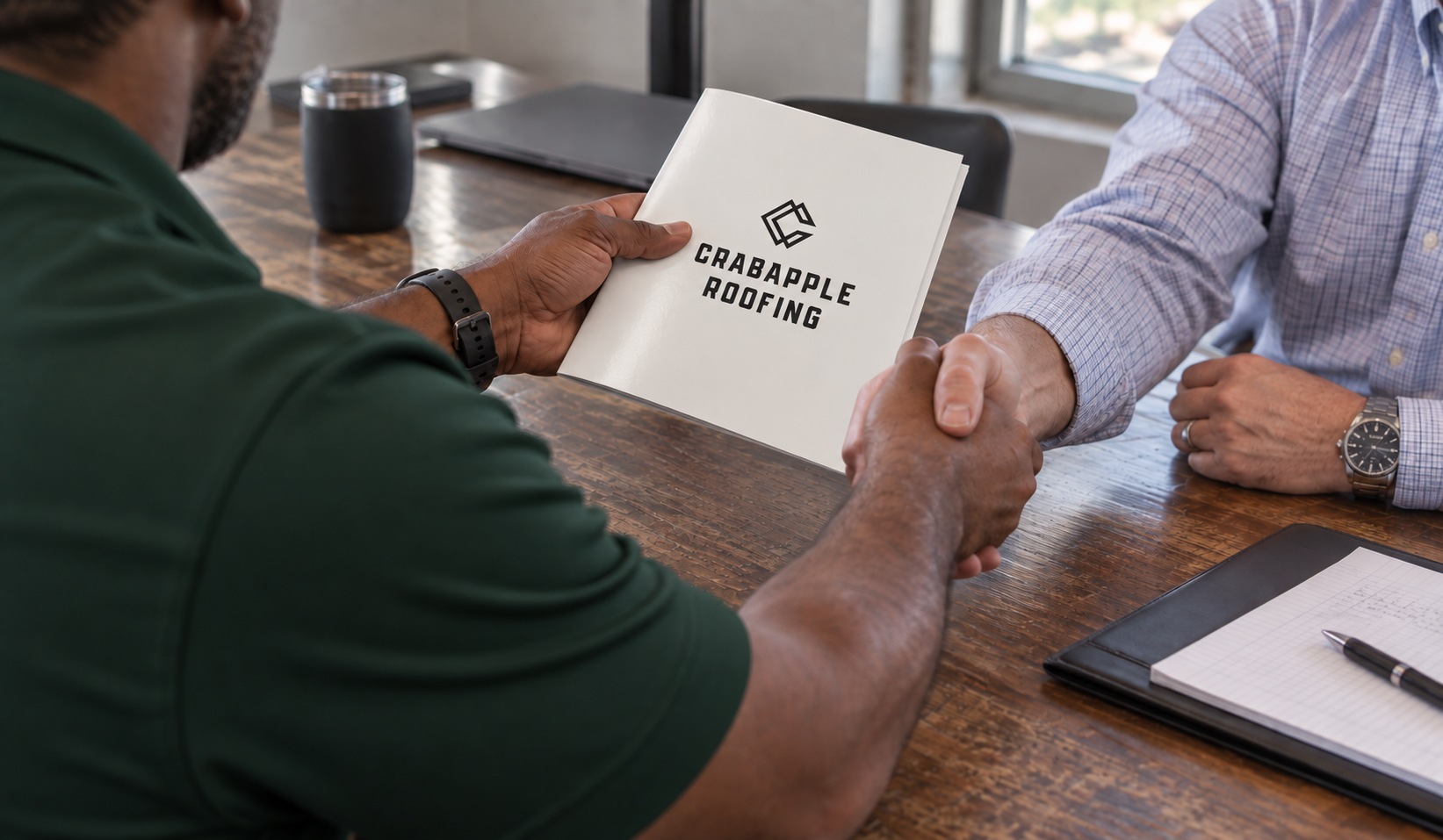 Crabapple Roofing representative shaking hands with a commercial client across a conference table while reviewing a Crabapple Roofing brochure