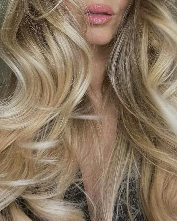 Close-up of a woman with long, wavy blonde hair and pink lipstick.