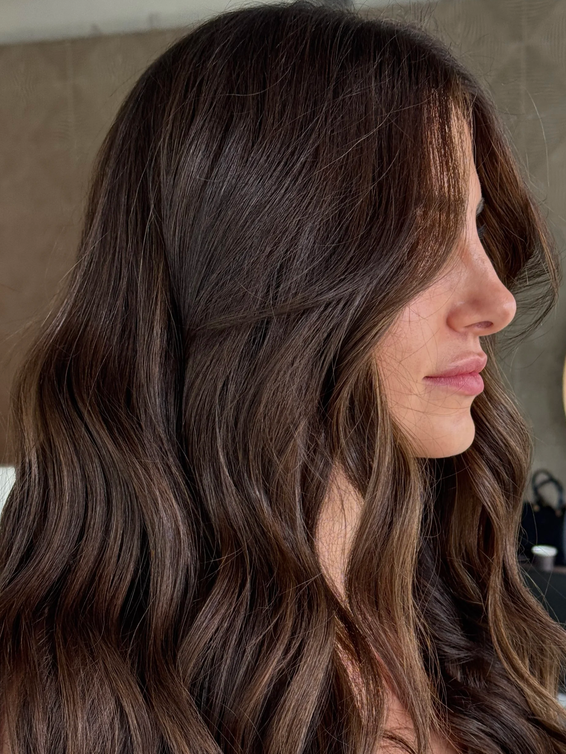 Profile of a woman with long, wavy brown hair, facing to the right.