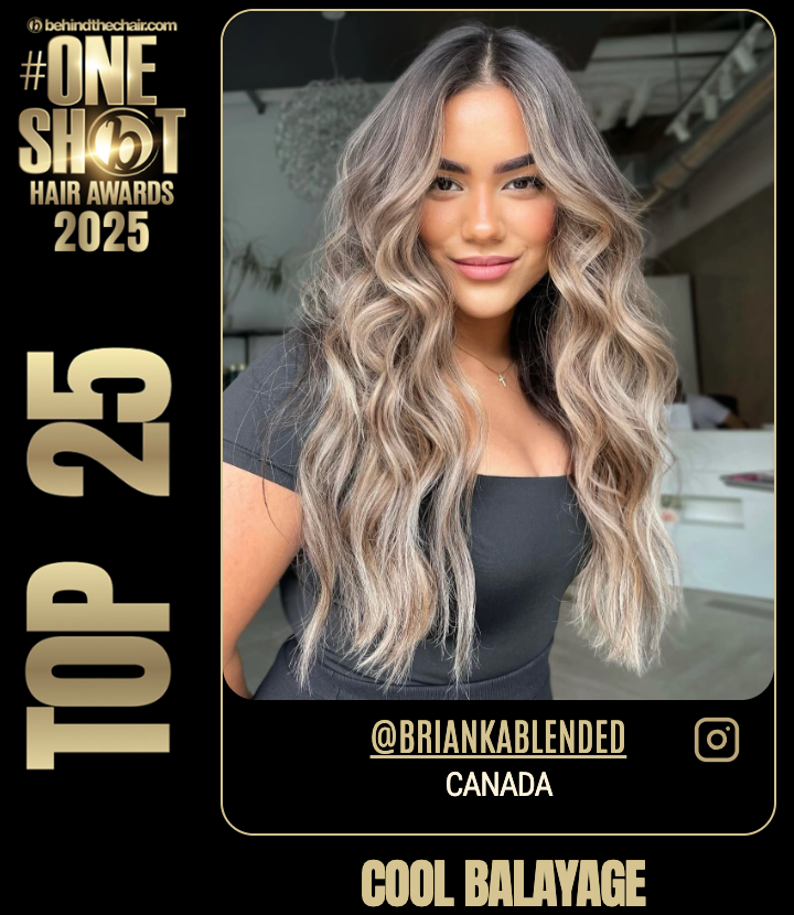 A young woman with long, wavy blonde and light brown hair smiling at the camera, wearing a black top, in a modern indoor setting.