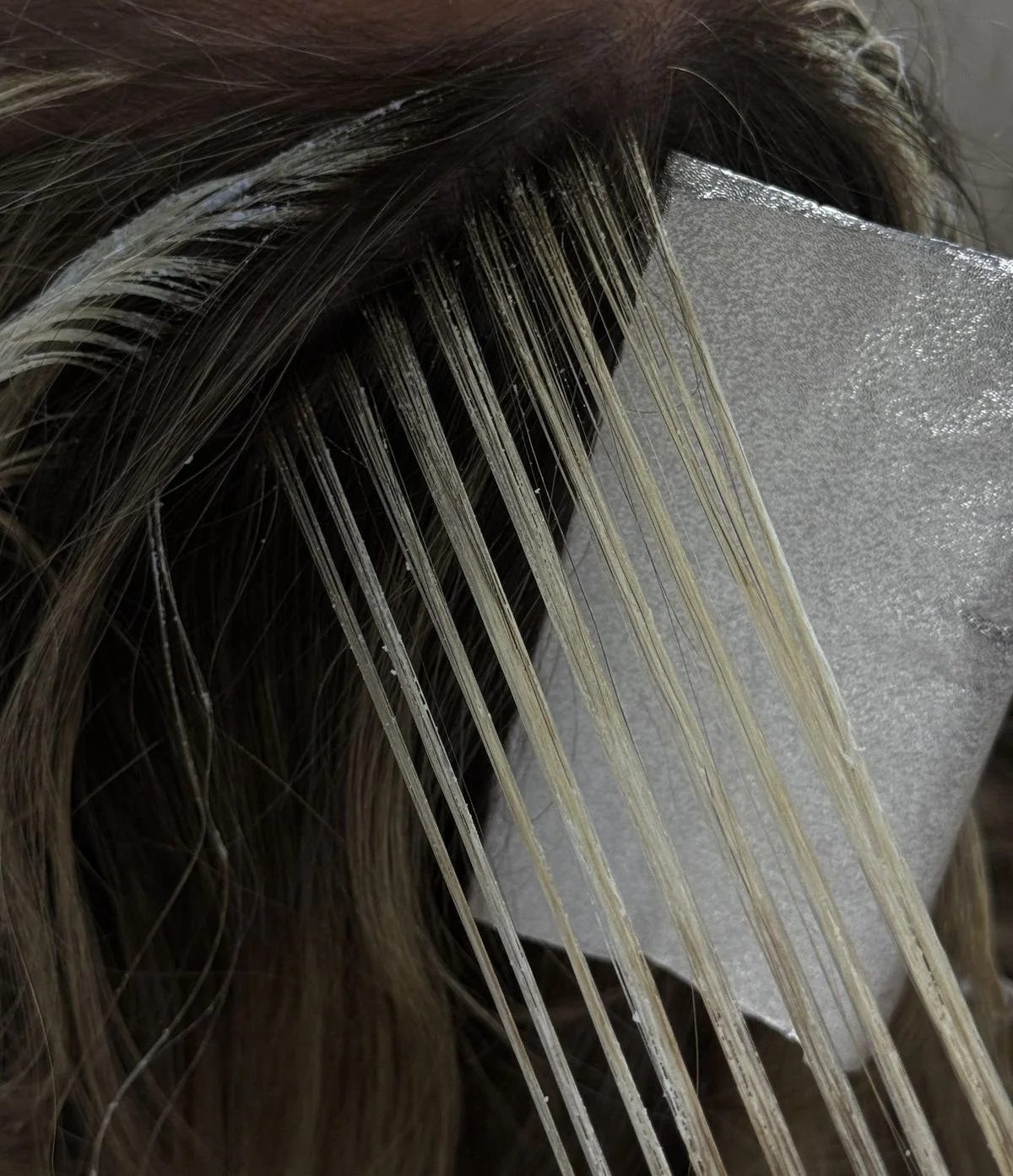 Close-up of a section of hair with a hairbrush or comb and a metallic object, possibly a hair clipper or mirror.