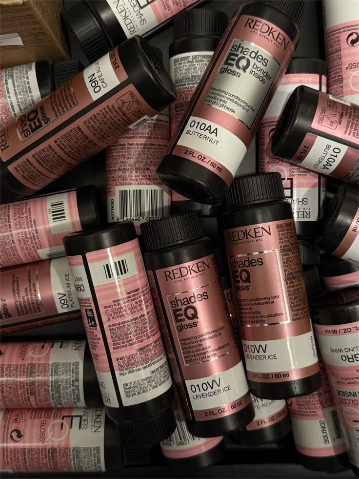 Pile of Redken Shades EQ Gloss hair dye bottles in various shades, including Lavender Ice and Butternut.