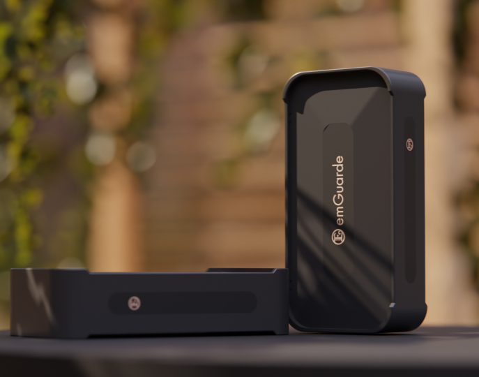 A black emGuarde device on a flat surface outdoors during daytime with wooden steps and greenery in the background.