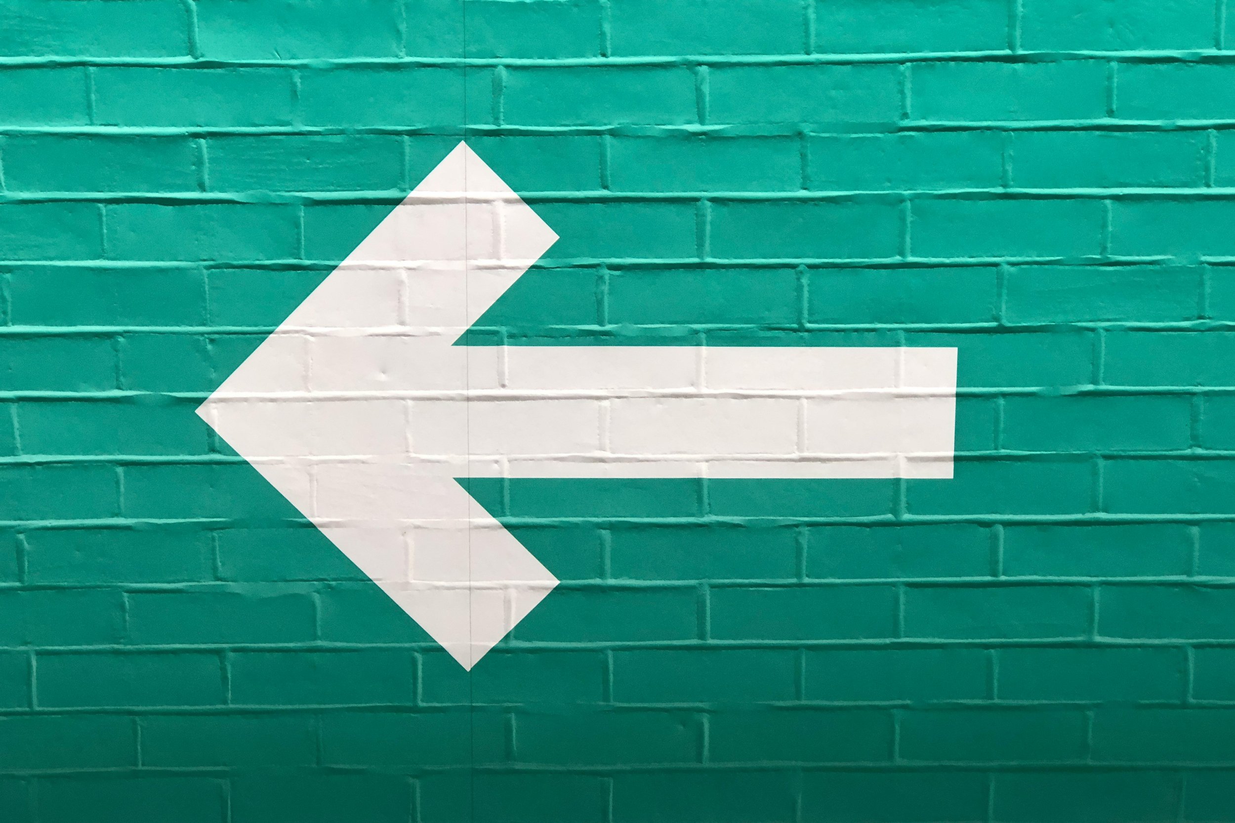 White directional arrow painted on a teal brick wall