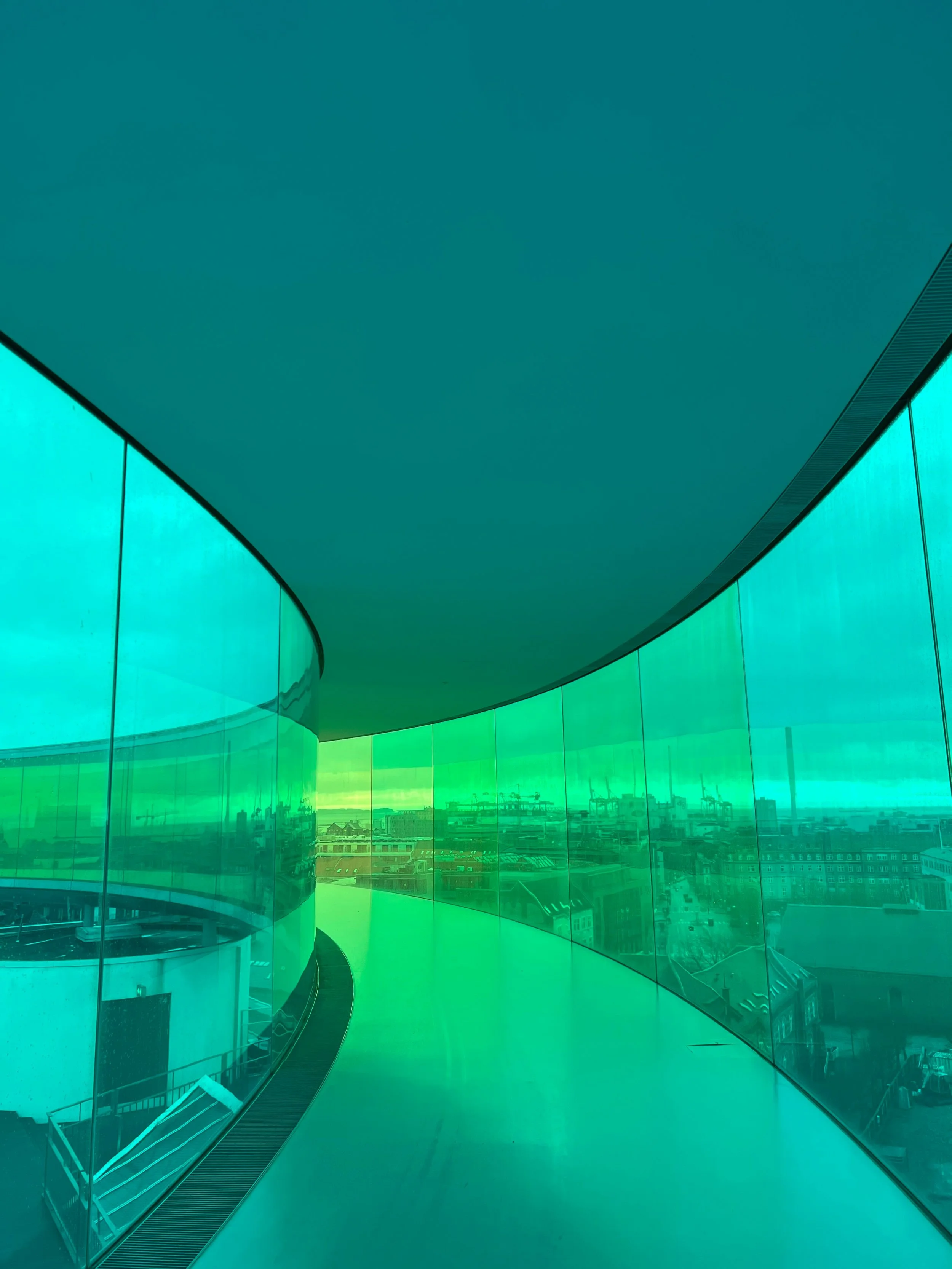 Interior view of a curved glass walkway with a teal-tinted city panorama below