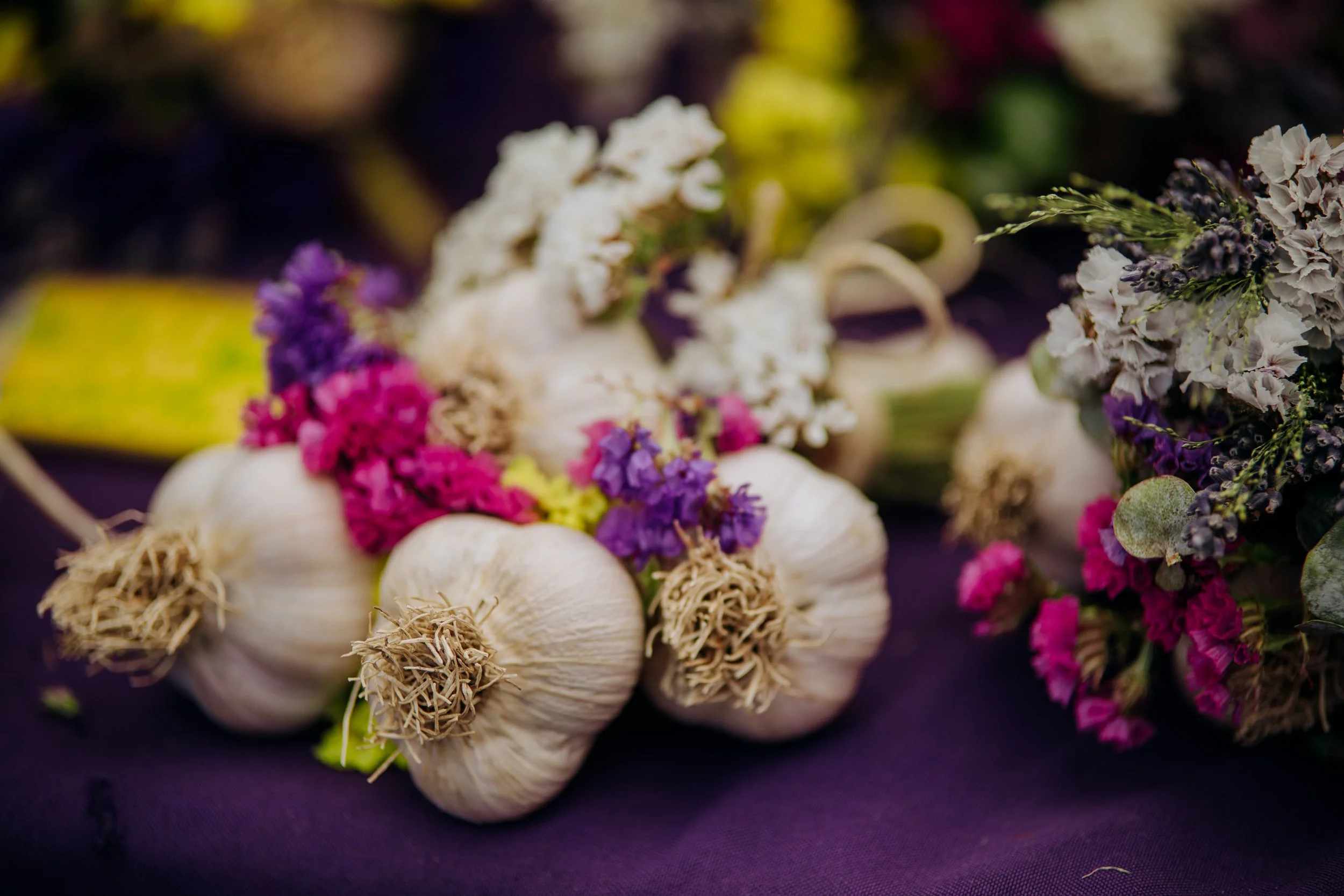 Fresh garlic bulbs arranged with purple, white, pink, and green flowers on a dark surface.