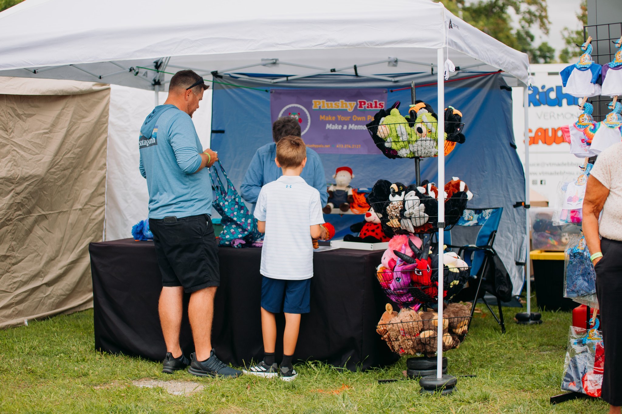 People shopping at a craft booth with plush toys and puppets at an outdoor fair.