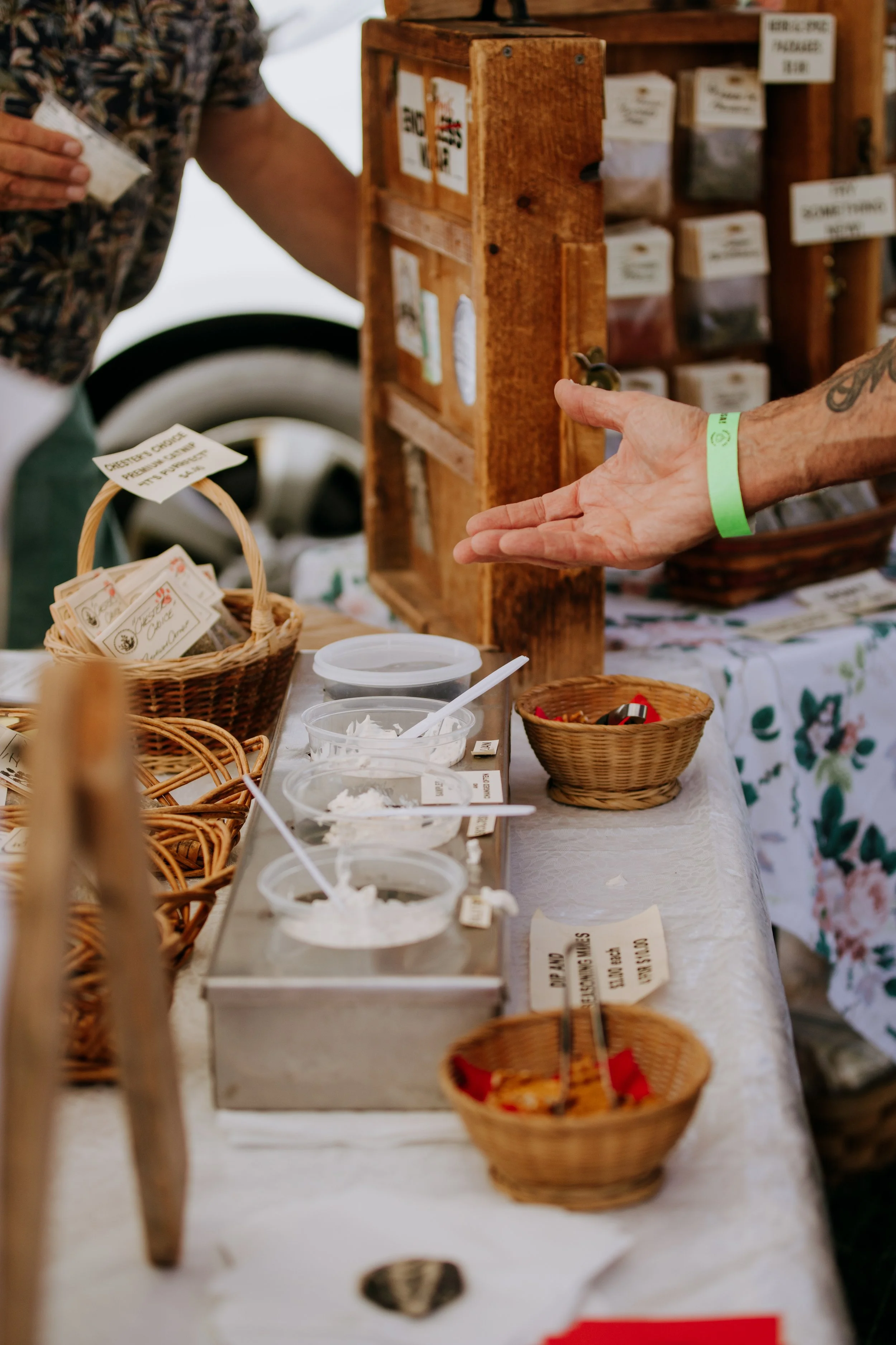 People purchasing spices or herbs at a market stall with small bowls of ingredients, labeled baskets, and a wooden display rack.