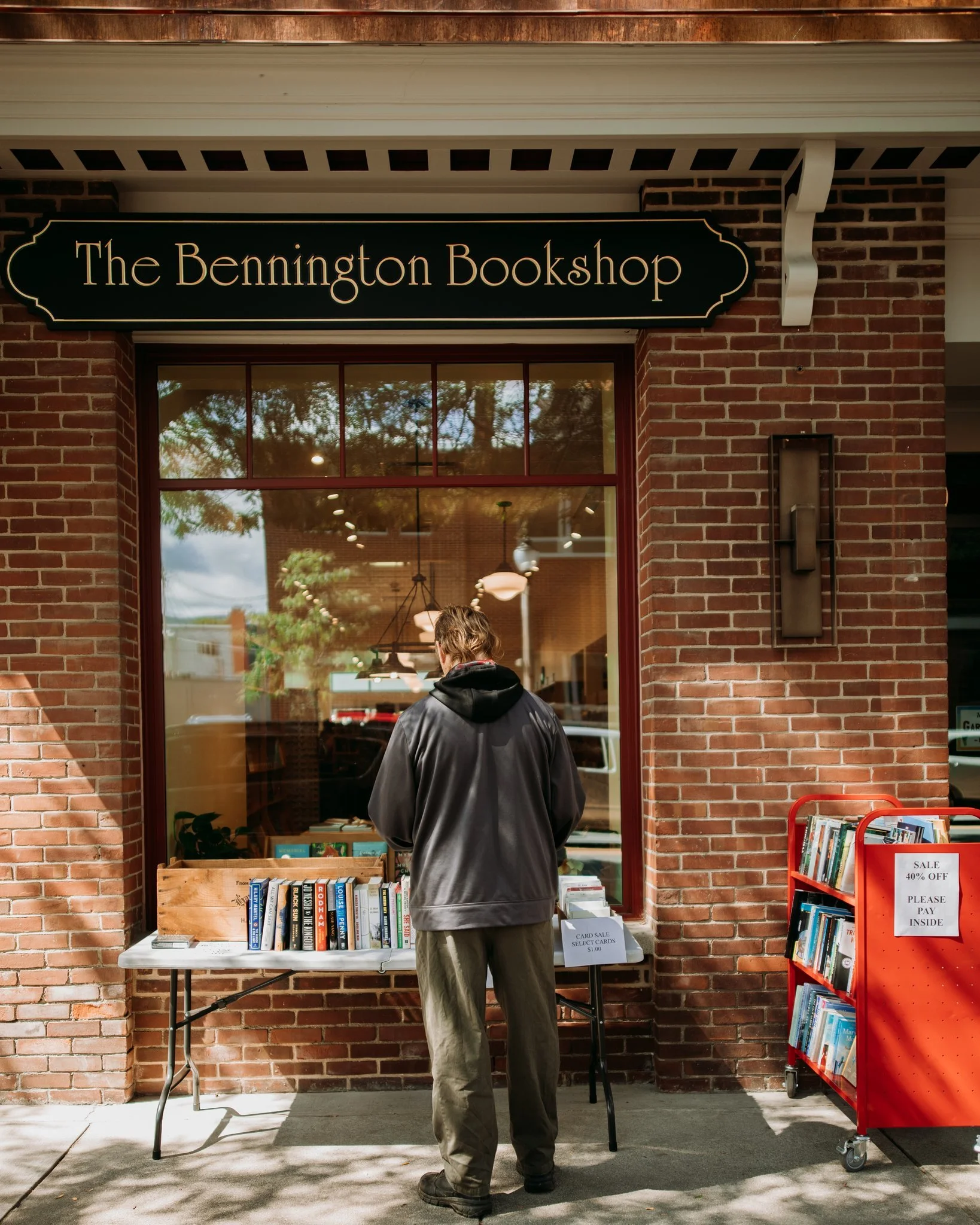 A man standing outside The Bennington Bookshop browsing books displayed on a table overlooking the sidewalk.