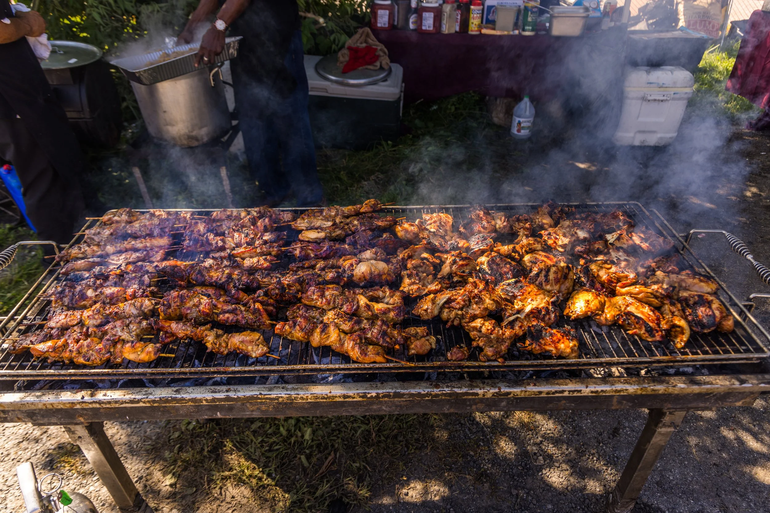 A large outdoor grill with various skewers and pieces of meat, cooking and producing smoke, at a food stall or outdoor market.