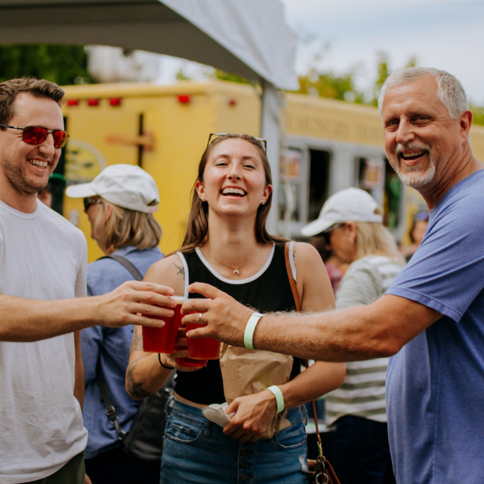 People enjoying drinks at an outdoor event or festival, smiling and clinking red cups.