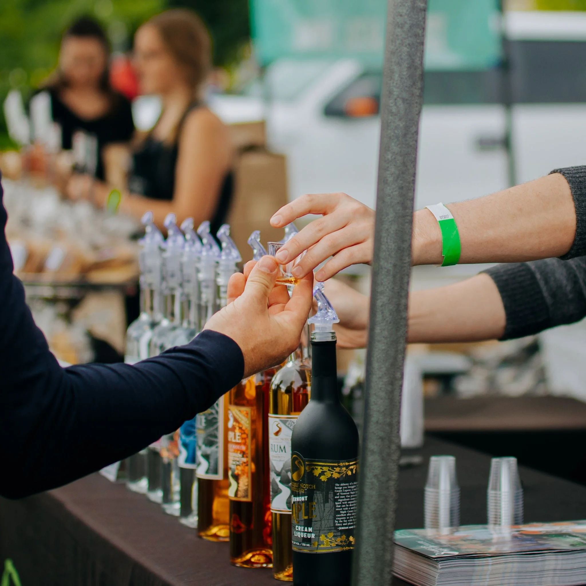 Person pouring liqueur into a shot glass at a booth with various bottles of alcohol on display.