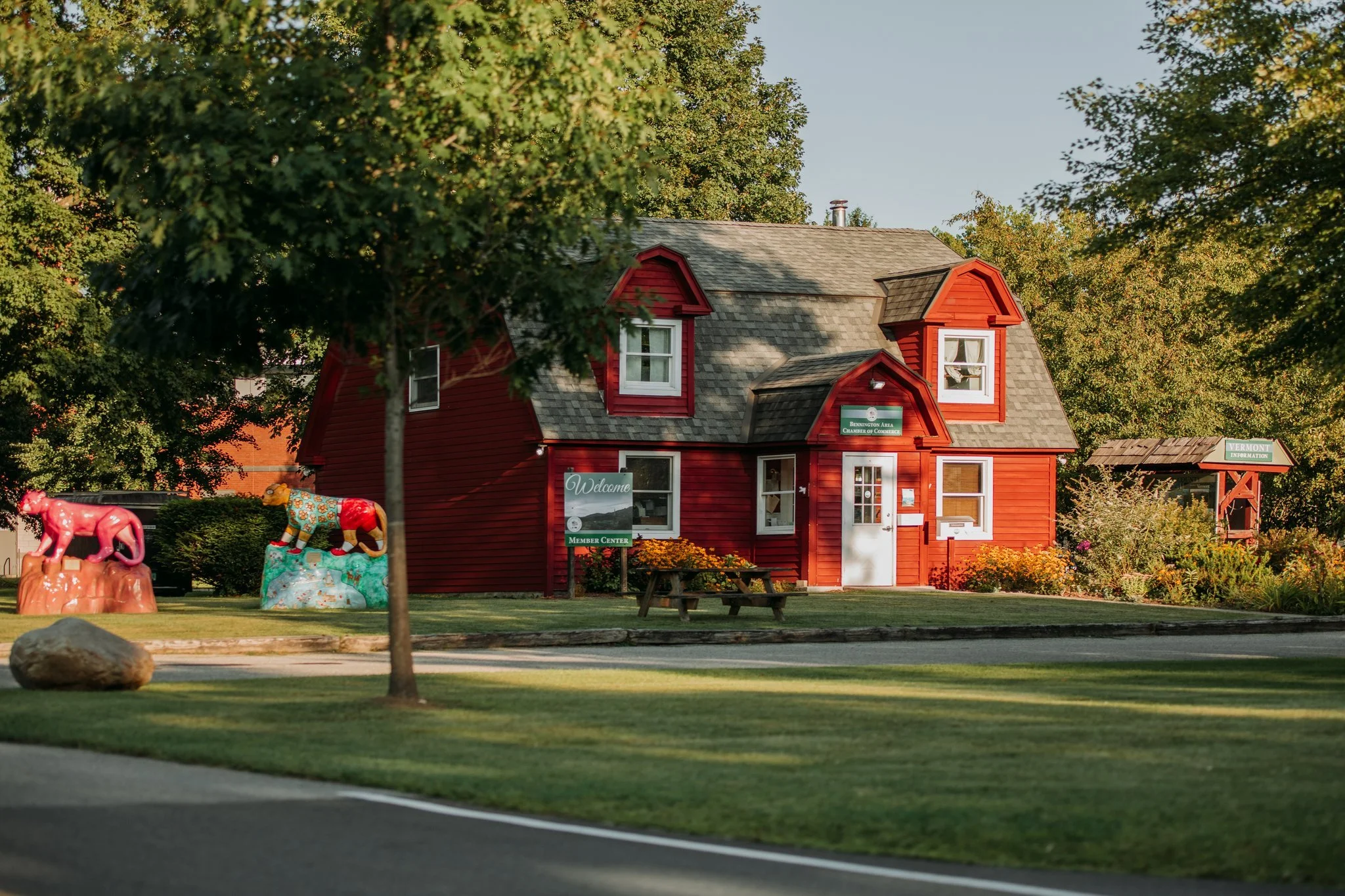 A red wooden building with white doors and windows, surrounded by green trees and grass, with decorative animal statues in front.