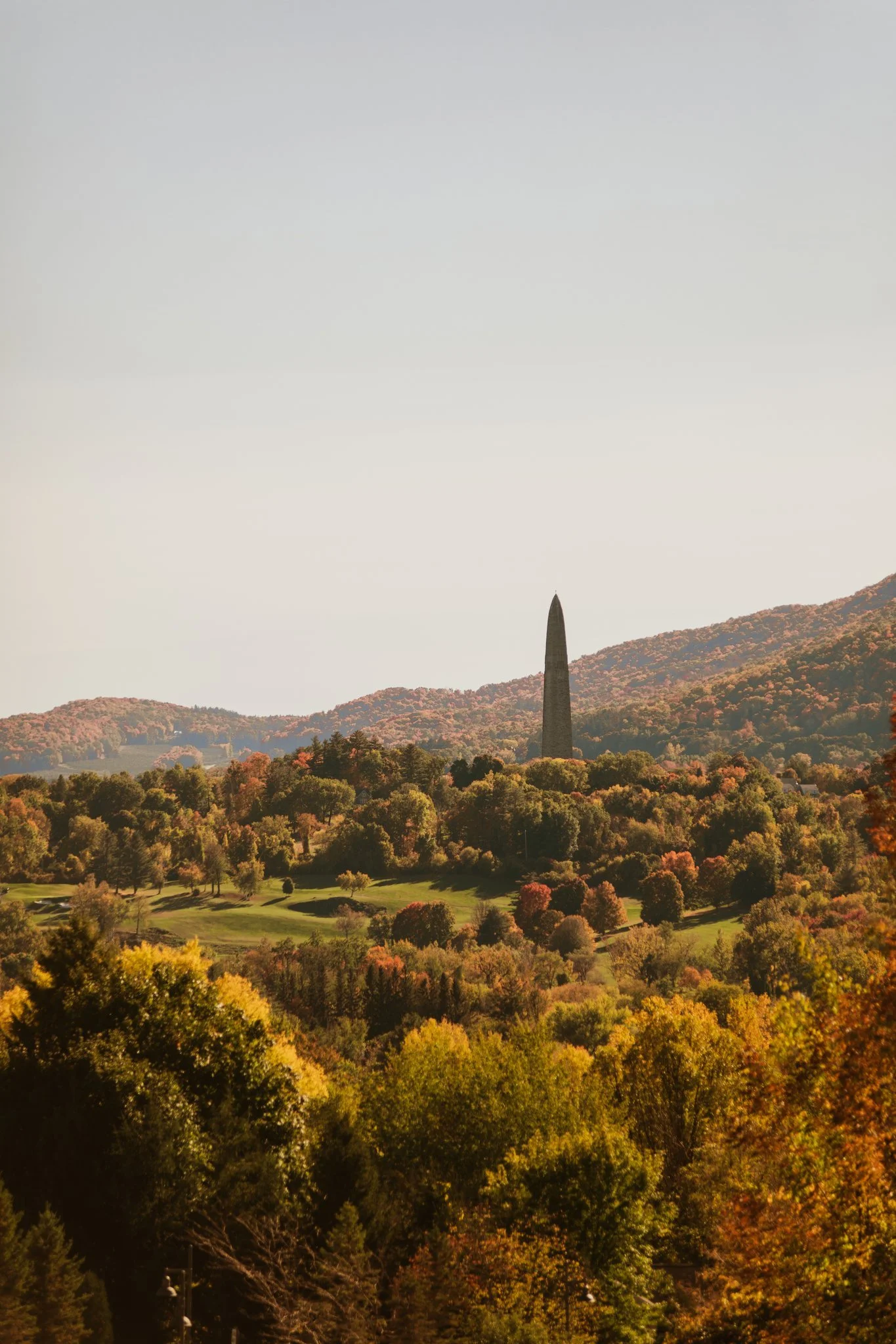Scenic landscape with fall foliage, rolling hills, and the Washington Monument in the distance under a clear sky.
