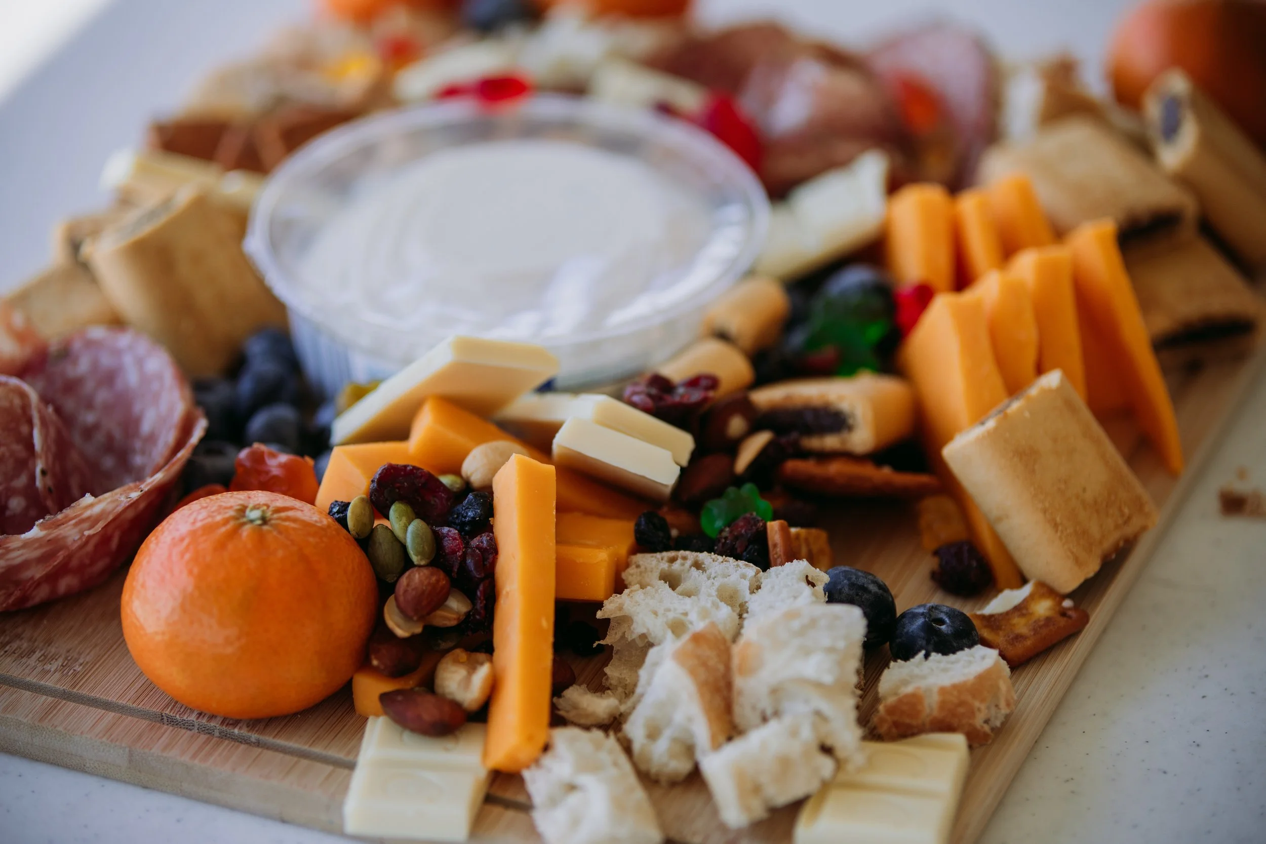 A cheese and charcuterie board with assorted cheeses, cured meats, fresh fruit, nuts, and a small bowl of dipping sauce.