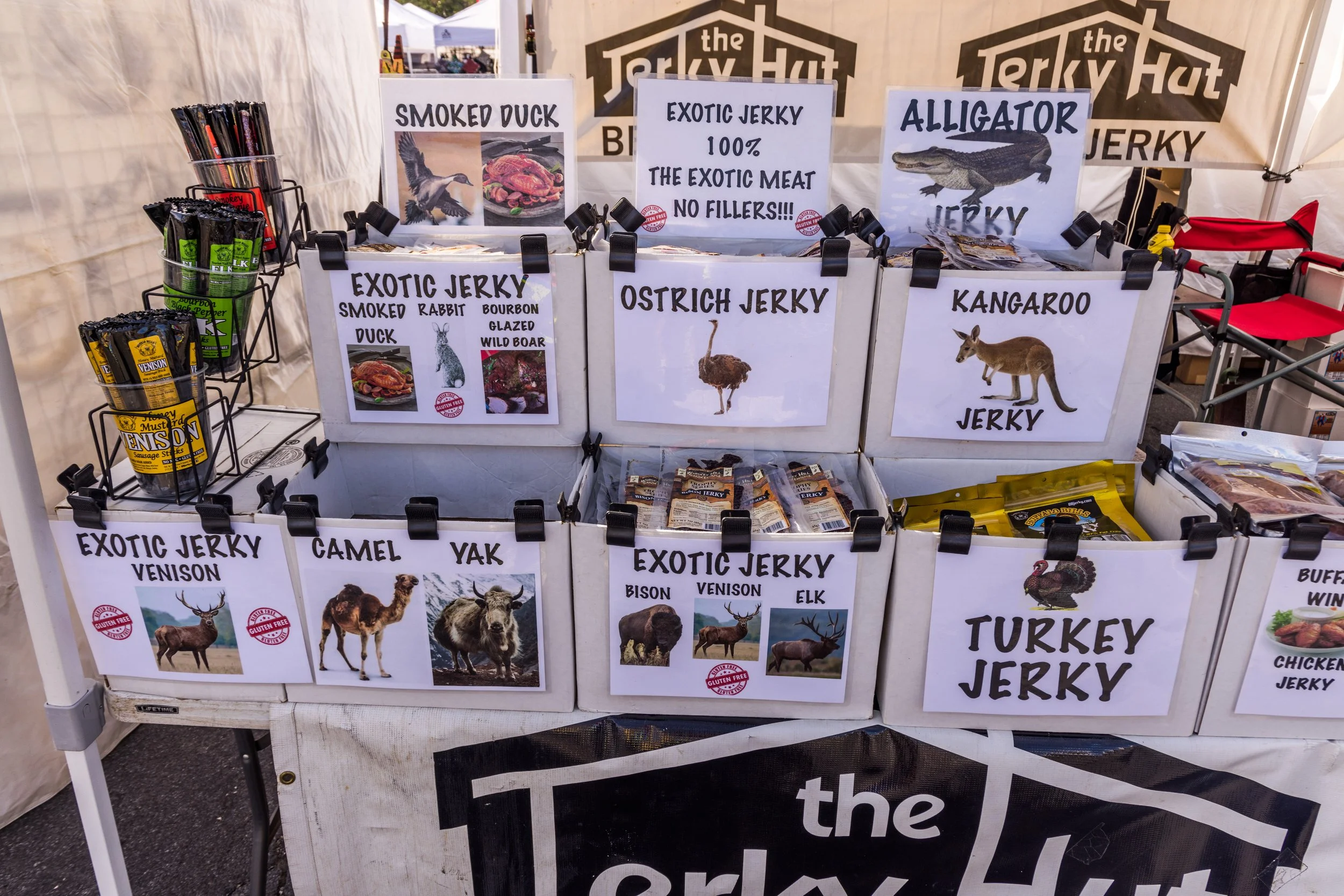 A display booth selling various types of jerky, including smoked duck, exotic rabbit, camel, yak, beef, elk, and turkey, with signs and pictures of each meat.