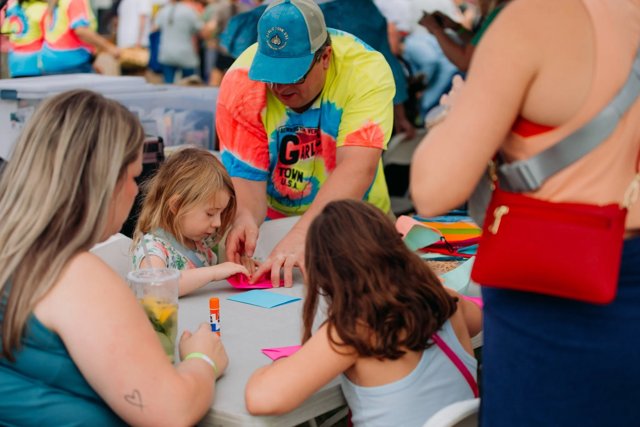 Children and adults making crafts at a table during an outdoor event.