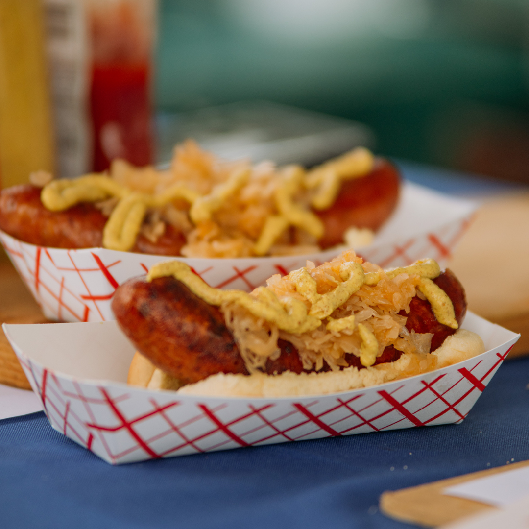 Two hot dogs in paper baskets, topped with relish and mustard, served on a blue table.