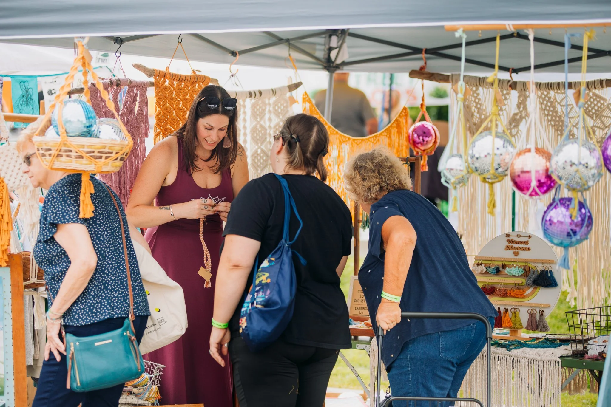 Women browsing handmade crafts and jewelry at an outdoor market stall.